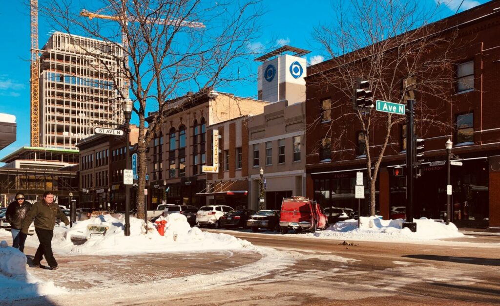 A street view of downtown Fargo, North Dakota, during winter. People walk past historic storefronts at 1st Ave N and Broadway, illustrating the vibrant business environment supported by the competitive North Dakota corporate tax rate.