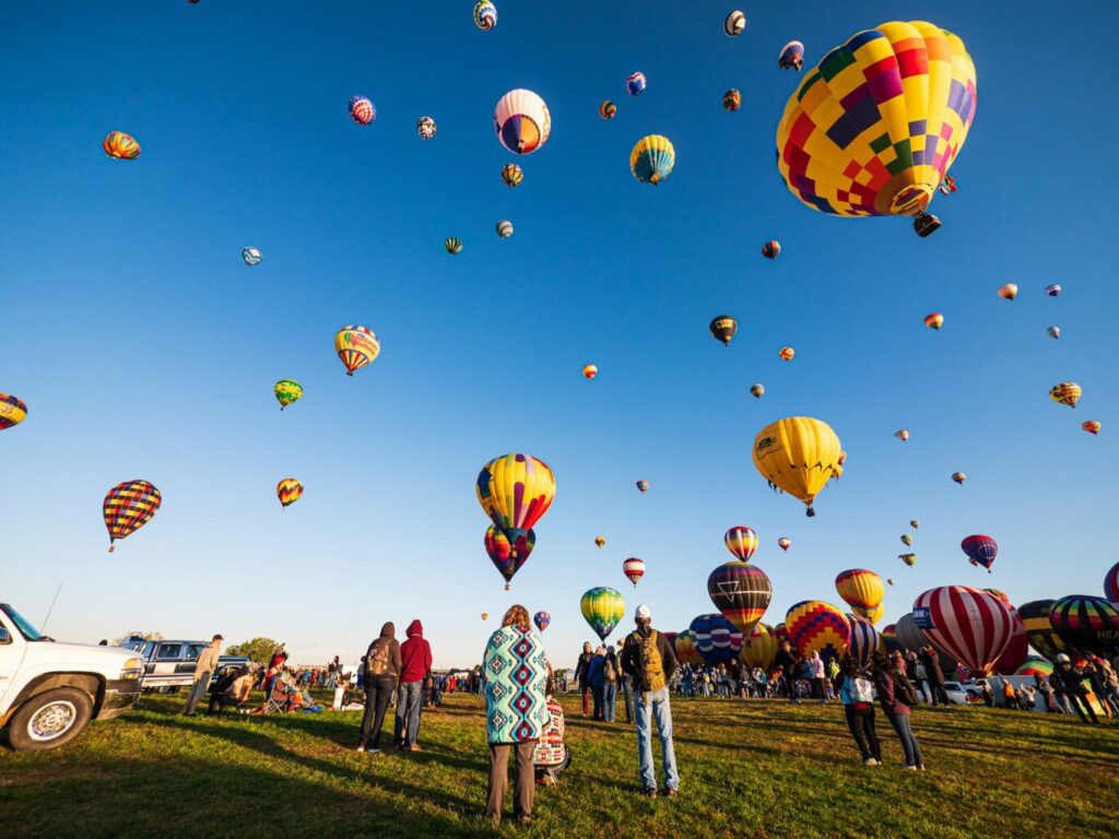 Multiple hot air balloons on green grass field under the blue sky.
