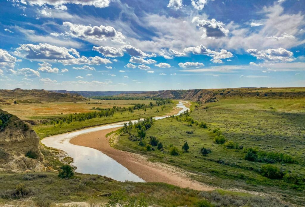 A river running through a lush green valley. Photographed in heodore Roosevelt National Park, North Dakota, USA