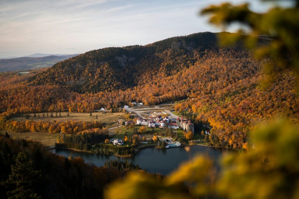 Scenic photograph of buildings by lake surrounded by mountains and trees.