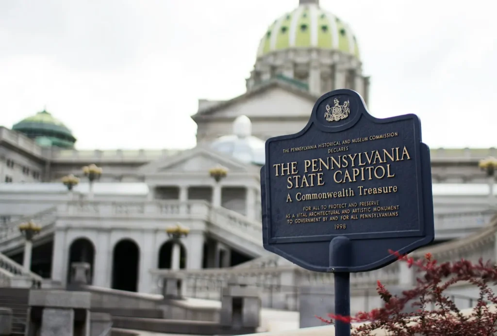 An informative sign for the Pennsylvania State Capitol building, a key site for state legislation and the Pennsylvania corporate tax rate decisions, with the historic dome and architectural details of the capitol in the blurred background.
