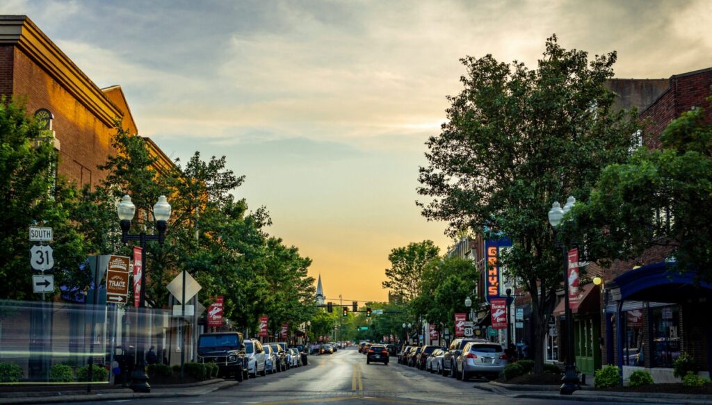 Tree-lined main street in Franklin, Tennessee at golden hour, with brick storefronts, parked cars, and a church steeple visible in the distance