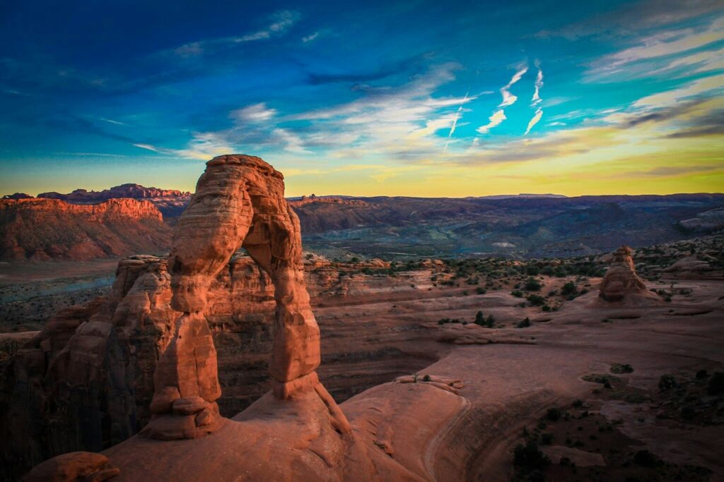 Delicate Arch standing against a vivid sunset sky in Arches National Park, Utah, with red rock canyon landscapes stretching into the distance